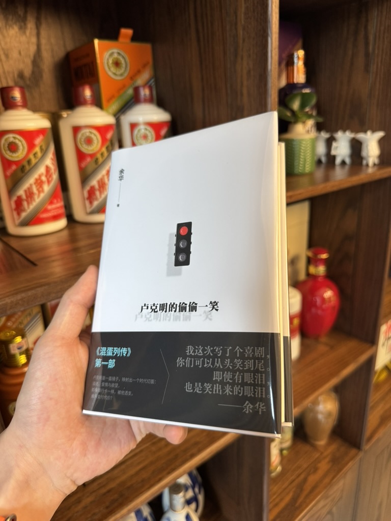 A hand holds Yu Hua’s Lu Keming’s Secret Smile in front of wooden shelves lined with bottles.